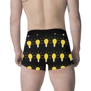 May include: Black boxer briefs with a repeating pattern of yellow light bulbs with white bases. The light bulbs have yellow radiating lines. The waistband is black.
