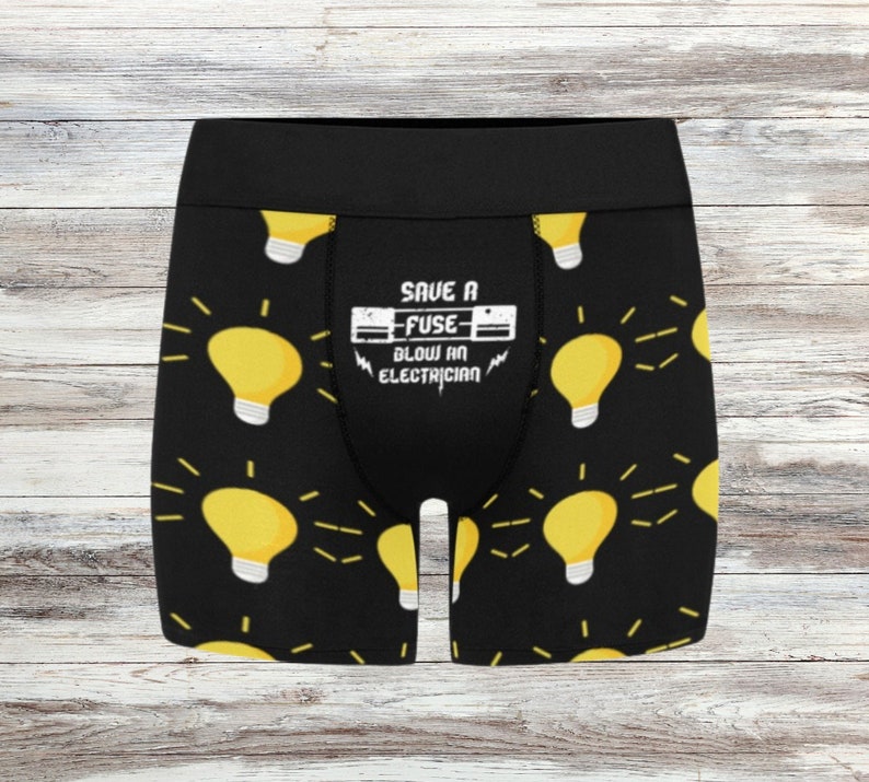 May include: Black boxer briefs with a repeating pattern of yellow light bulbs with white bases and radiating lines. The waistband is black. The front of the briefs has the text "SAVE A FUSE BLOW AN ELECTRICIAN" in white.