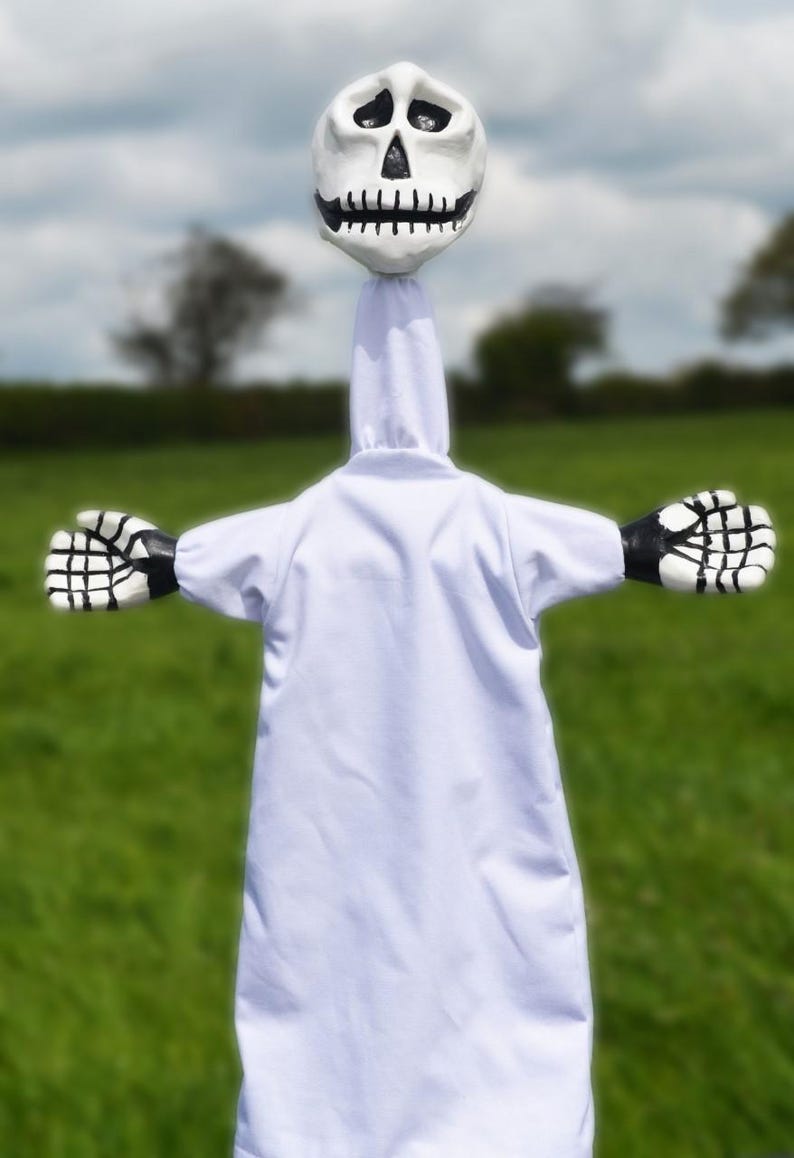 K&ouml;nnte beinhalten: Ein wei&szlig;es Geisterkost&uuml;m mit einem Sch&auml;delkopf und schwarzen und wei&szlig;en Skeletth&auml;nden. Der Geist steht auf einem grasbewachsenen Feld.