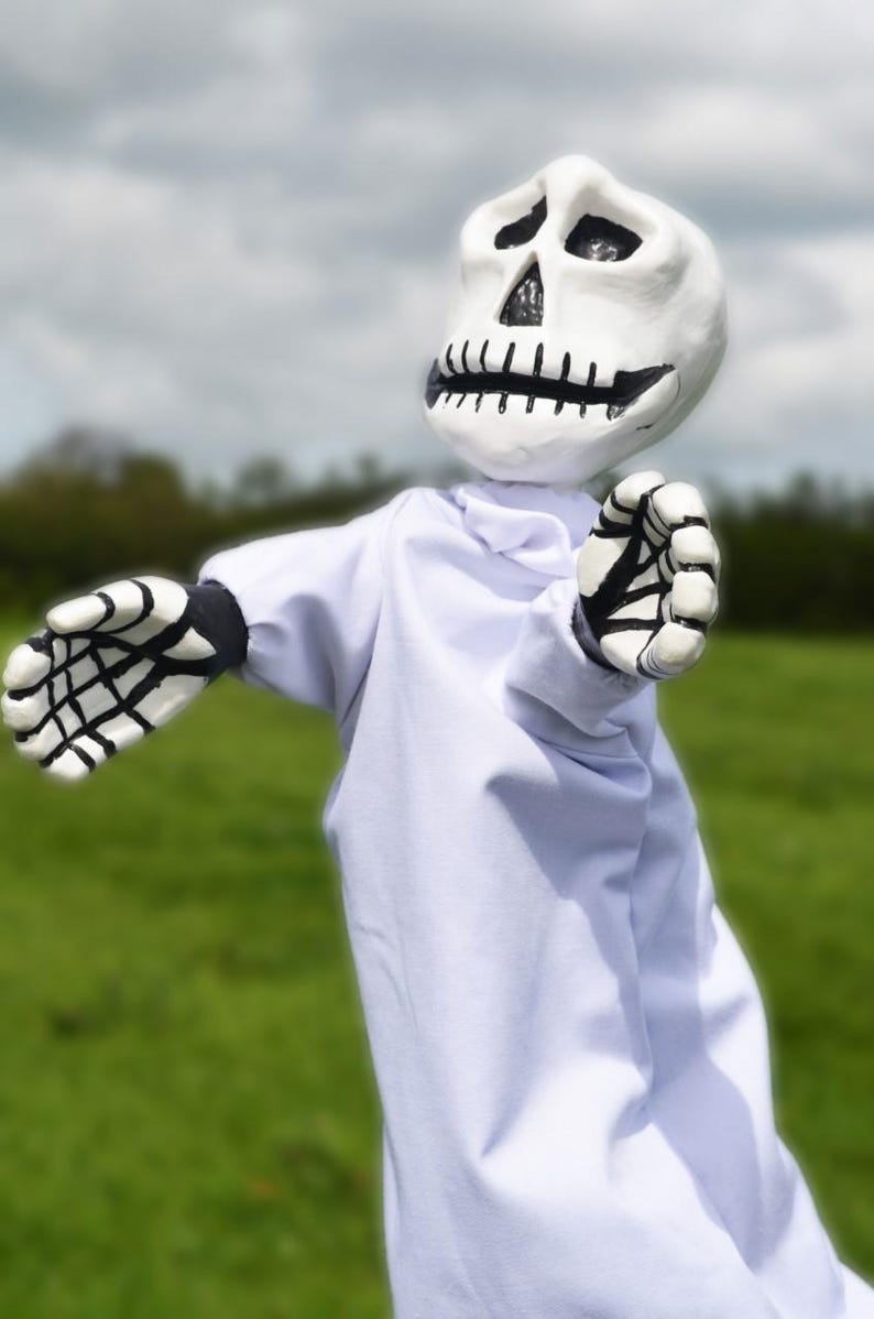K&ouml;nnte beinhalten: Eine wei&szlig;e Skelettpuppe, die eine wei&szlig;e Robe mit schwarzen Skeletth&auml;nden tr&auml;gt. Die Puppe hat ein bemaltes Sch&auml;delgesicht mit schwarzen Augen und einem schwarzen Mund.