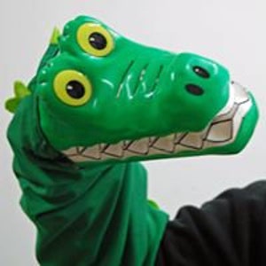May include: Green hand puppet shaped like an alligator with large yellow eyes and a toothy grin.