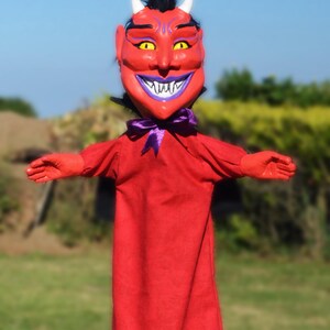 May include: Red devil puppet with a purple bow tie and horns. The puppet has a large, toothy grin and is made of felt.