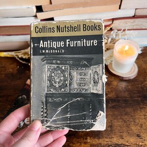 May include: A vintage book titled "Collins Nutshell Books - Antique Furniture" by J.W. McDonald. The cover features a black and white photograph of an ornately carved antique cabinet.