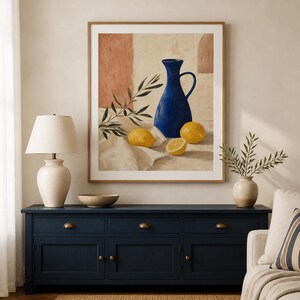 May include: A framed wall art print featuring a still life painting of a vibrant blue pitcher, three yellow lemons, and a green olive branch resting on a white cloth against a textured background with warm terracotta and cream color tones.