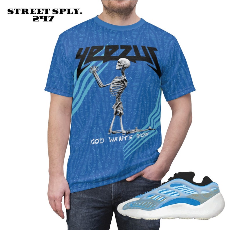 Puede incluir: Una camiseta azul con un gr&aacute;fico de esqueleto y el texto "YEEZY" y "GOD WANTS YOU". La camiseta se combina con zapatillas azules y blancas.