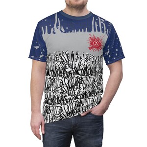 Puede incluir: Una camiseta blanca con un patr&oacute;n de salpicaduras azul y blanco. La camiseta tiene un dise&ntilde;o de graffiti en blanco y negro en la parte delantera y un logotipo rojo con el texto "A" y "Art" en la parte posterior.