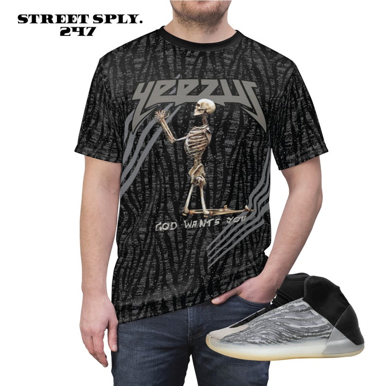 May include: A black and grey t-shirt featuring a skeleton graphic and the text "YEEZUS" and "GOD WANTS YOU". The person is wearing blue jeans and black and grey trainers.