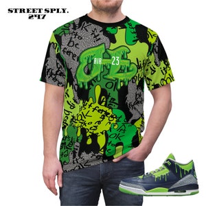Puede incluir: Una camiseta negra con un estampado de graffiti verde y negro con el texto "AIR 23". Un par de zapatillas verdes y negras con un efecto de pintura que gotea.