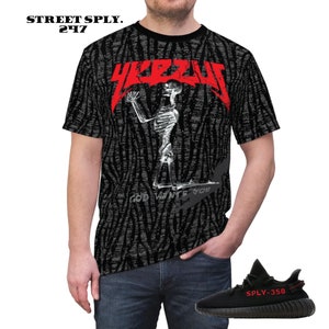 Puede incluir: Camiseta negra y blanca con un logotipo "YEEZY" rojo y un gr&aacute;fico de esqueleto. El texto "GOD WANTS YOU" est&aacute; impreso debajo del esqueleto. La camiseta se combina con zapatillas negras y rojas con el texto "SPLY-350" en el lateral.