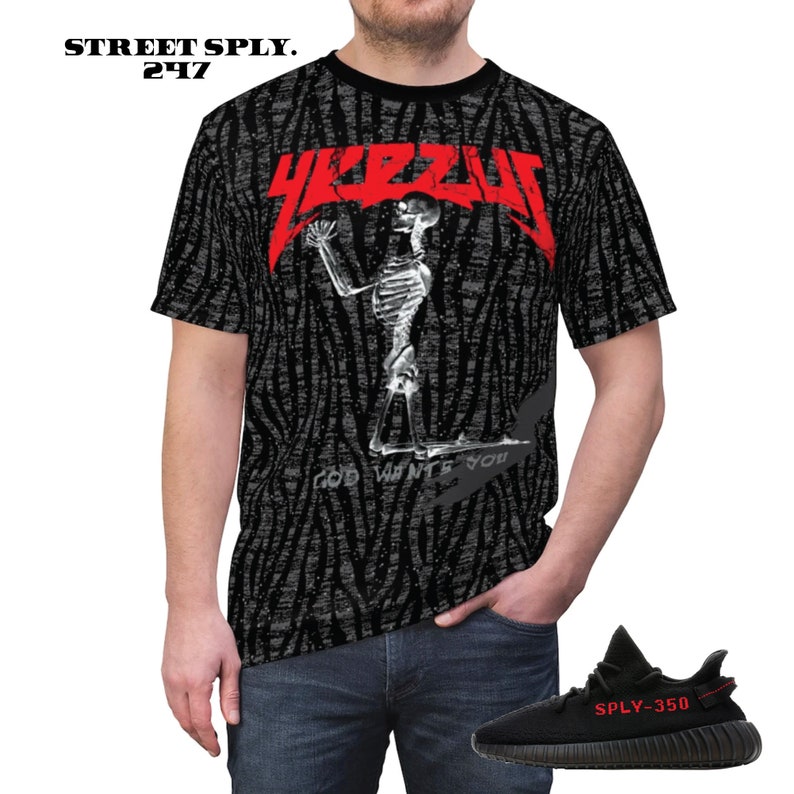 Puede incluir: Camiseta negra y blanca con un logotipo "YEEZY" rojo y un gr&aacute;fico de esqueleto. El texto "GOD WANTS YOU" est&aacute; impreso debajo del esqueleto. La camiseta se combina con zapatillas negras y rojas con el texto "SPLY-350" en el lateral.