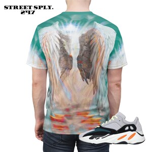 K&ouml;nnte beinhalten: Ein t&uuml;rkisfarbenes Batik-T-Shirt mit einem Motiv von Engelsfl&uuml;geln. Die Fl&uuml;gel sind wei&szlig; und grau mit einem Licht, das durch sie scheint. Das T-Shirt wird mit wei&szlig;en, schwarzen und orangefarbenen Turnschuhen kombiniert.