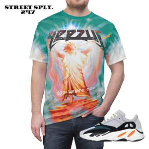 K&ouml;nnte beinhalten: Ein t&uuml;rkisfarbenes Batik-T-Shirt mit einem grafischen Aufdruck eines Engels mit dem Text "God Wants You" und dem Wort "Yeezus" in einer verwitterten Schriftart. Die Person tr&auml;gt eine blaue Jeans und wei&szlig;e, schwarze und orangefarbene Turnschuhe.