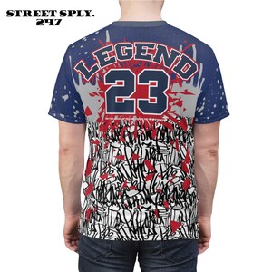 Puede incluir: Una camiseta azul, blanca y roja con un dise&ntilde;o de graffiti y el texto "LEGEND 23" en la espalda.
