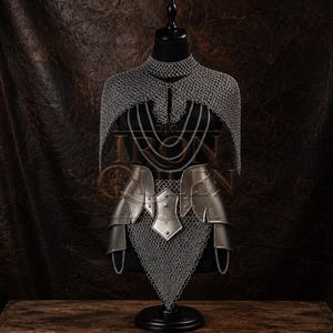 May include: A silver-toned metal chainmail mantle and waist armor set featuring a high collar, draped chain accents, and a pointed front panel. The armor includes smooth, curved metal plates at the waist with visible rivets and a chainmail skirt.