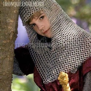 May include: A person wearing a chainmail hood and a burgundy tunic with a gold-coloured sword. The image includes the text "IRONQUEENARMORY" in the upper left corner. The person is leaning against a tree.