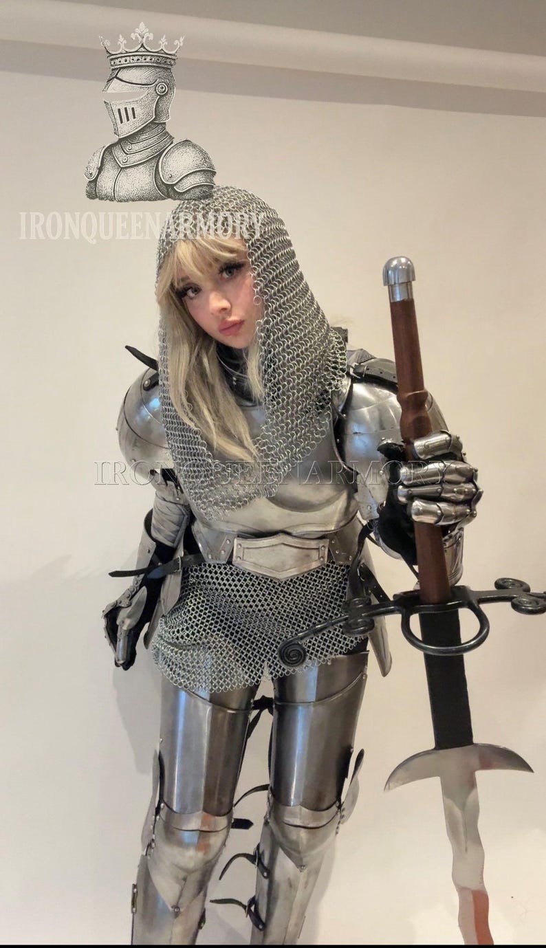 May include: A person in full silver armour, including a chainmail hood, shoulder plates, and leg guards, holding a long sword with a brown handle. The image includes the text "IRONQUEENARMORY".