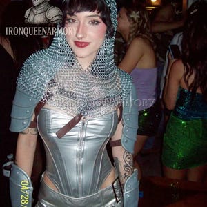 May include: A silver corset and skirt ensemble, complemented by arm guards and a chainmail hood. The image features the text "IRONQUEENARMORY" and the date "04/28/2007". The outfit is reminiscent of medieval armor.