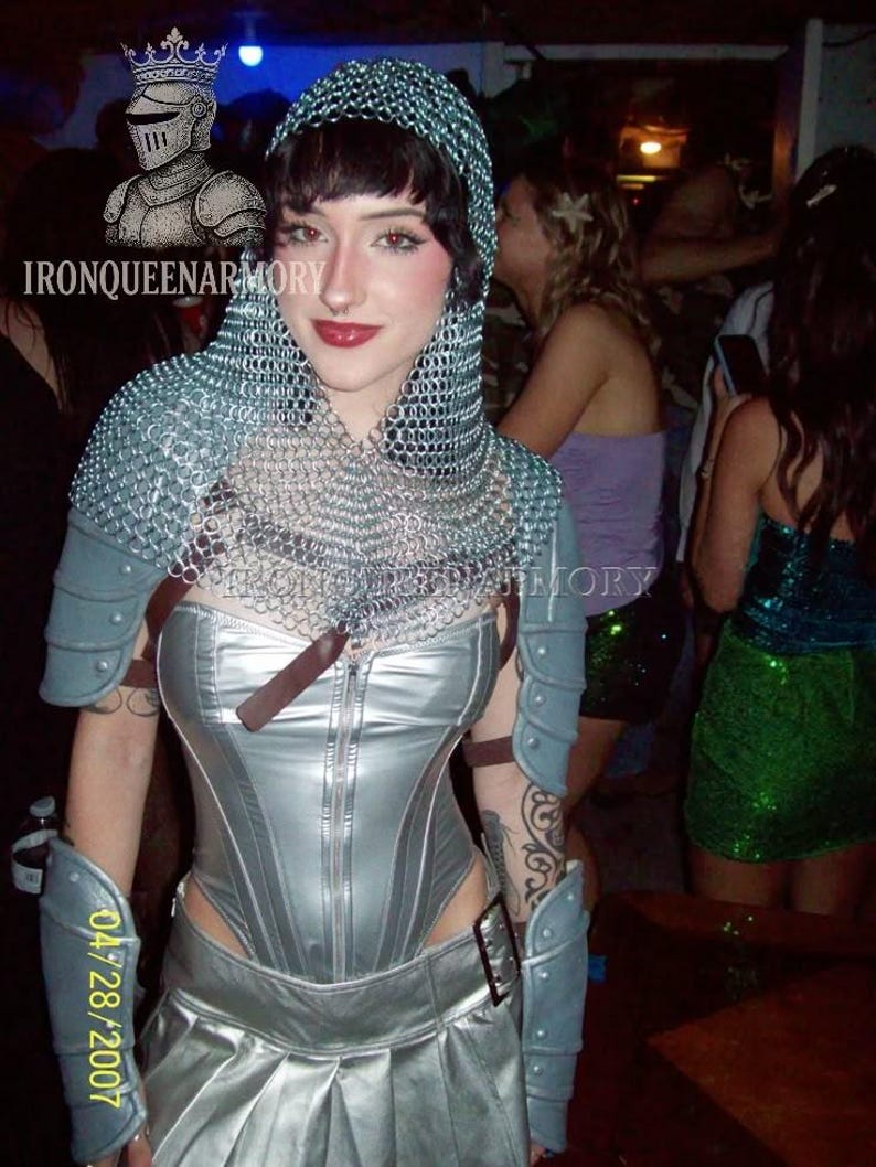 May include: A silver corset and skirt ensemble, complemented by arm guards and a chainmail hood. The image features the text "IRONQUEENARMORY" and the date "04/28/2007". The outfit is reminiscent of medieval armor.