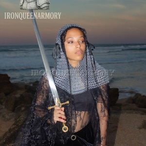 May include: A person holding a long sword with a gold hilt and a silver blade. The person is wearing a chainmail hood and a black lace cape. The image includes the text "IRONQUEENARMORY".