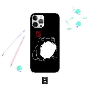 May include: Black phone case with a white frog outline and a large open mouth. The case has a red stamp design and the word "OPPEA" in a vertical font. Pencils and paperclips are scattered around the phone.