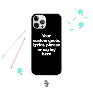 May include: Black phone case with the text "Your custom quote, lyrics, phrase or saying here" in white. Pencils, paper clips, and an eraser are scattered around the case.