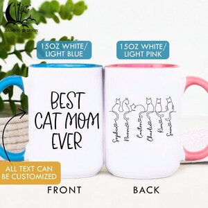 May include: Two white ceramic mugs with black text and cat illustrations. One mug has a blue interior and handle, the other has a pink interior and handle. The front mug reads "BEST CAT MOM EVER". The back mug has cat silhouettes and names.
