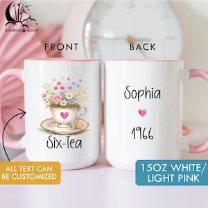 May include: White ceramic mug with a pink handle and interior. The front features a floral teacup design with the text "Six-Tea." The back displays the name "Sophia," a pink heart, and the year "1966." The mug is labeled "15OZ WHITE/ LIGHT PINK."