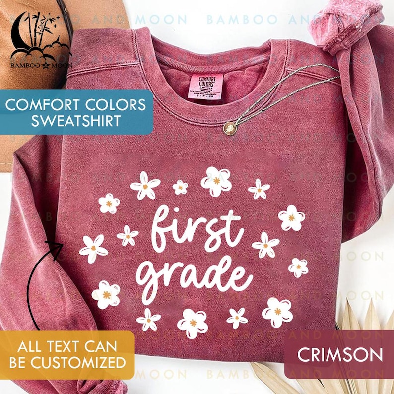 May include: Crimson Comfort Colors sweatshirt with white floral accents and the words "first grade." The sweatshirt also has the text "Comfort Colors Sweatshirt" and "All text can be customized."