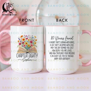 May include: White ceramic mug with a pink handle and rim, featuring floral artwork and the text "CHAPTER EIGHTY Sophia" on the front. The back of the mug has the text "80 Years Loved" and a poem.