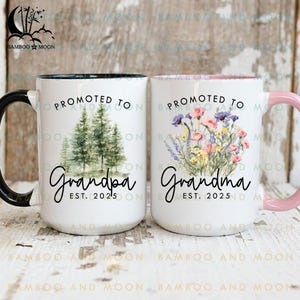 Peut inclure: Deux tasses en céramique blanche avec des bords noirs et roses. La tasse de gauche a une scène de forêt et le texte "Promu Grand-père Est. 2025". La tasse de droite a un motif floral et le texte "Promue Grand-mère Est. 2025".