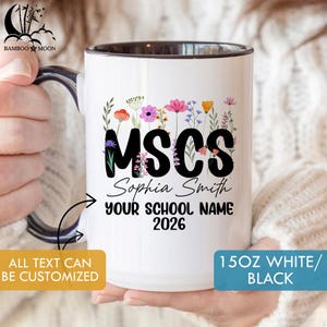 Könnte beinhalten: Weißer Keramikbecher mit schwarzem Innenraum und Henkel. Der Becher zeigt den Text "MSCS" in großen schwarzen Buchstaben, mit dem Namen "Sophia Smith" und "YOUR SCHOOL NAME 2026" darunter. Florale Illustrationen in verschiedenen Farben verzieren die Oberseite. Der Becher ist 444 ml.