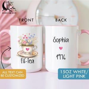 May include: A white ceramic mug with a pink handle and interior. The front features a floral teacup design with the text "Fif-Tea". The back displays the name "Sophia", a heart, and the year "1976". The mug is 15 oz.