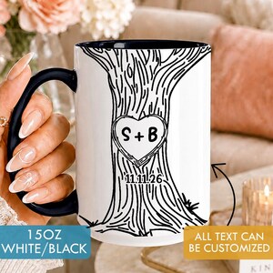 Peut inclure: Un mug en céramique blanche avec un intérieur et une anse bleu foncé, orné d'un dessin au trait noir représentant un tronc d'arbre avec un cœur gravé contenant les lettres S + B et la date 11.11.26, avec une capacité de 15oz indiquée.