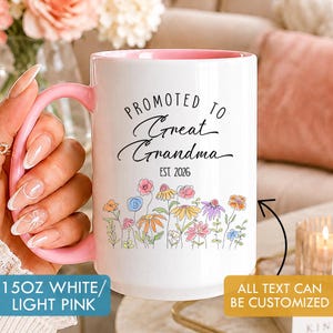May include: A 444 ml white ceramic mug with a light pink interior and handle. The front features a floral illustration in various colours above the black text PROMOTED TO Great Grandma EST. 2026. The mug includes a label stating 15OZ WHITE/LIGHT PINK.