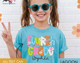 May include: A lagoon blue t-shirt with the words "Fourth Grade" in colorful, playful lettering. The name "Sophia" is printed below. The shirt is worn by a person wearing blue sunglasses and making a peace sign.