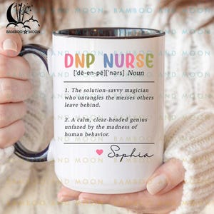 Può includere: Una tazza in ceramica bianca con bordo e manico neri. La tazza presenta una grafica colorata che recita "DNP Nurse [de-en-pe][nǝrs] Noun" e include una definizione del termine. La tazza è personalizzata con il nome "Sophia" in rosa.