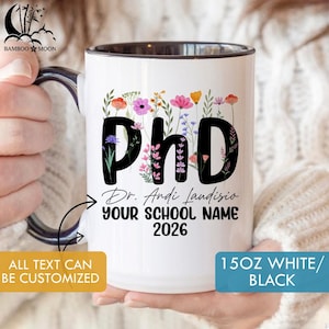 Könnte beinhalten: Weißer Keramikbecher mit schwarzem Innenraum, mit dem Wort "PhD" in Schwarz und floralen Akzenten. Der Becher enthält auch den Text "Dr. Andi Landisio", "YOUR SCHOOL NAME" und "2026". Der Becher ist 425 ml.