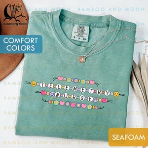 May include: Seafoam green t-shirt with the words "Telemetry Nurse" spelled out with decorative beads, hearts, flowers, and peace signs. The shirt also has the words "Comfort Colors" printed on it.