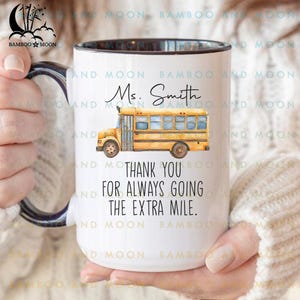 May include: White ceramic mug with a black rim and handle. The mug features a yellow school bus illustration and the text "Ms. Smith, Thank you for always going the extra mile."