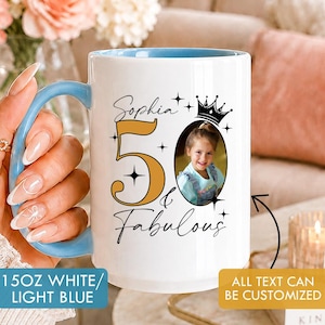 Puede incluir: Una taza de cerámica blanca de 444 ml con asa e interior azul claro. El diseño incluye el texto Sophia, 50 & Fabulous, un icono de corona y una foto de un niño en un marco ovalado. La taza tiene letras negras y el número 50 en dorado.