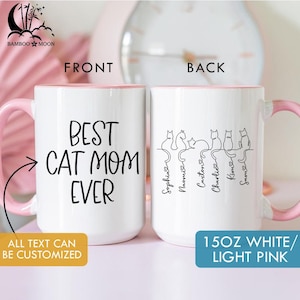 May include: White ceramic mug with a pink handle and interior rim. The front of the mug reads "BEST CAT MOM EVER" in black script. The back features cat silhouettes with names. The mug is 15 oz.