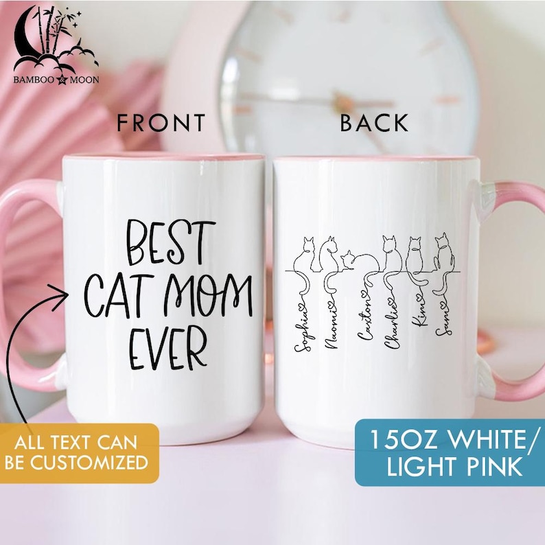 May include: White ceramic mug with a pink handle and interior rim. The front of the mug reads "BEST CAT MOM EVER" in black script. The back features cat silhouettes with names. The mug is 15 oz.