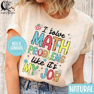 Op de afbeelding: Een beige T-shirt met de tekst "I solve MATH PROBLEMS like it's MY JOB" in kleurrijke, gepatroneerde letters. Het shirt heeft een natuurlijke afwerking.