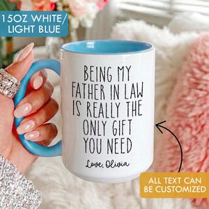 May include: White ceramic mug with a light blue interior and handle. The mug has the text "BEING MY FATHER IN LAW IS REALLY THE ONLY GIFT YOU NEED" in black. The text "Love, Olivia" is also on the mug. The mug is 15 oz.