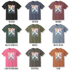 Pu&ograve; includere: Nove t-shirt di diversi colori con una grafica di una gabbia toracica con creature dei cartoni animati colorate al suo interno. Il testo "THORACIC PARK" &egrave; stampato su ogni t-shirt.