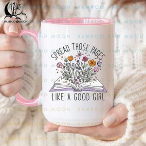 Pode incluir: Caneca de cerâmica branca com interior e alça rosa. A caneca apresenta o texto "SPREAD THOSE PAGES LIKE A GOOD GIRL" com uma ilustração floral de flores coloridas e um livro aberto.