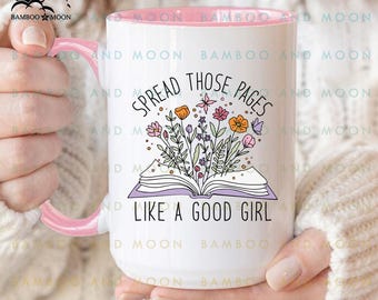 May include: White ceramic mug with a pink interior and handle. The mug features the text "SPREAD THOSE PAGES LIKE A GOOD GIRL" with a floral illustration of colorful flowers and an open book.