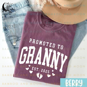 May include: A purple t-shirt with the text "Promoted to Granny Est. 2025" in white lettering. The shirt has a graphic of footprints and hearts.