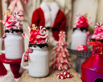 May include: A festive Christmas display featuring white Mason jar mugs with whipped cream toppings, candy canes, and gingerbread men. A red and white candy cane tree and a red birdhouse with "MERRY" text are also present.