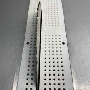 Może przedstawiać: Zbliżenie na biały wkład do piły stołowej z wystającym z środka okrągłym ostrzem piły. Wkład ma siatkę małych otworów.